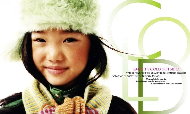 Close-up of a young girl wearing a fluffy green hat and a multicolored scarf, smiling at the camera.
