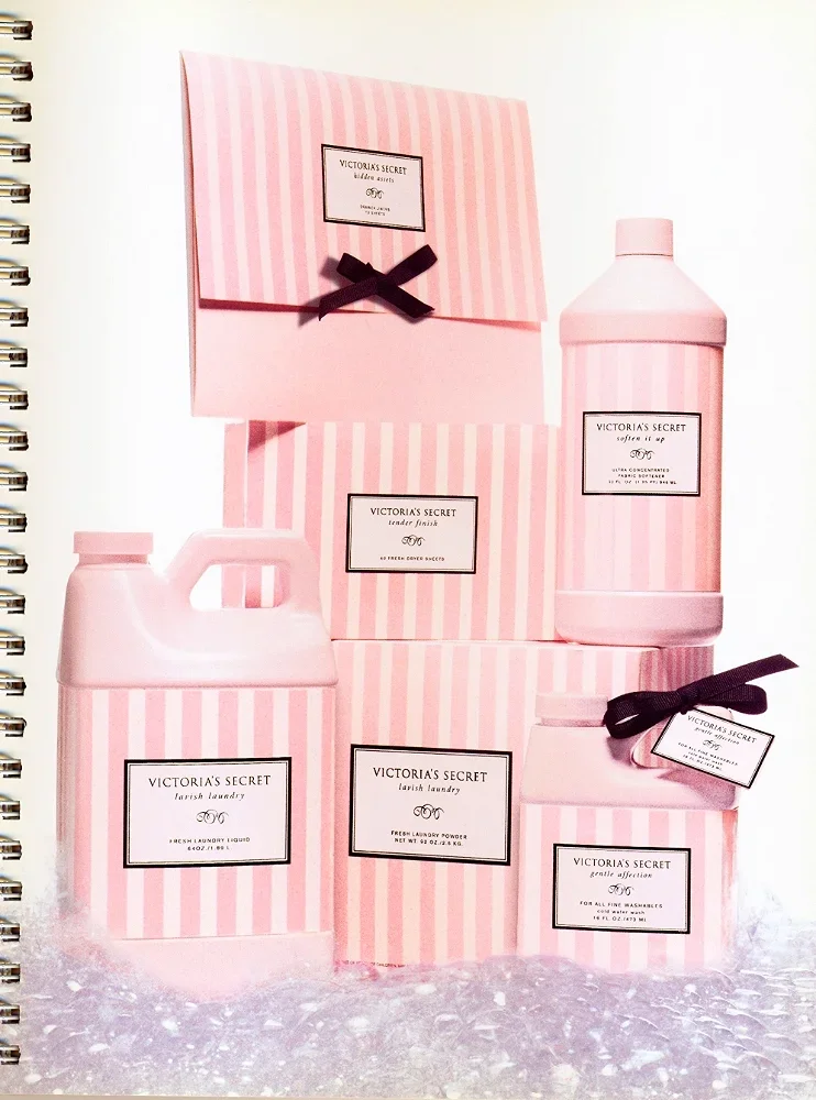 Victoria's Secret laundry and bath products in pink and white striped packaging, including detergent, fabric softener, laundry liquid, powder, and sachets, with some boxes tied with black ribbons.