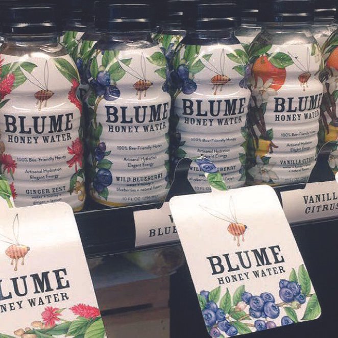 Bottles of Blume Honey Water on store shelf with labels featuring floral and berry designs and tags hanging in front.