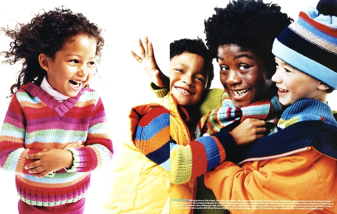 Four children smiling and playing together against a white background. Two boys and two girls wearing colorful sweaters and jackets.