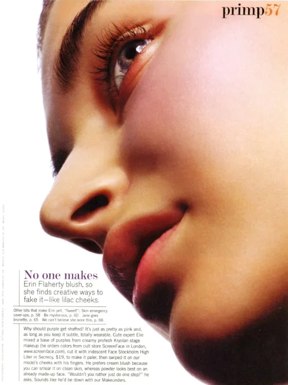 Close-up of a woman with a makeup artist's brush applying blush to her cheek, highlighting her eye, nose, and lips.