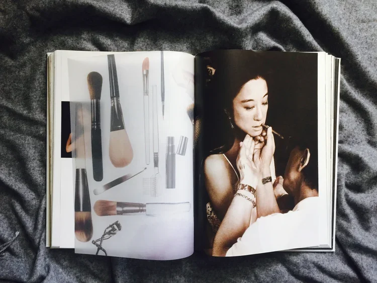 Open magazine showing makeup brushes and cosmetics on the left page and a woman applying makeup on the right page.