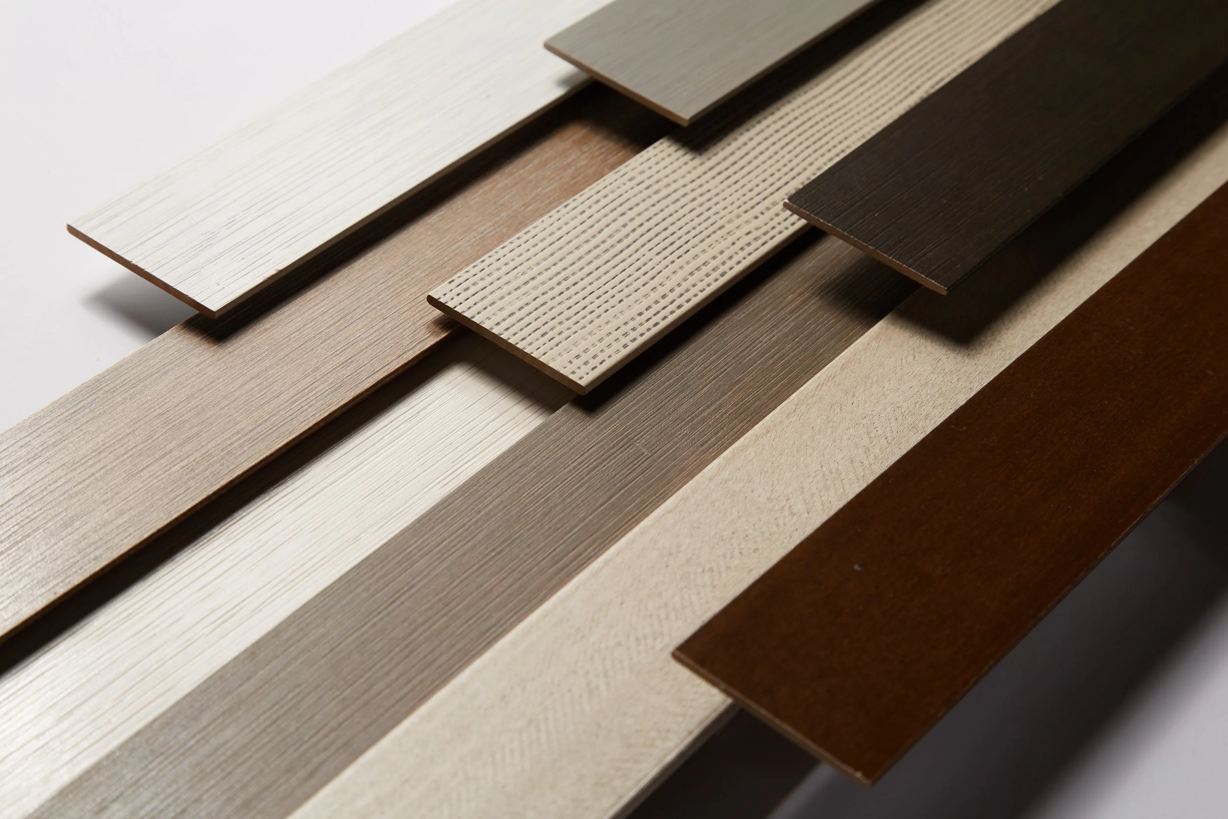 Various samples of wood or laminate flooring in different colors and finishes arranged in overlapping layers.