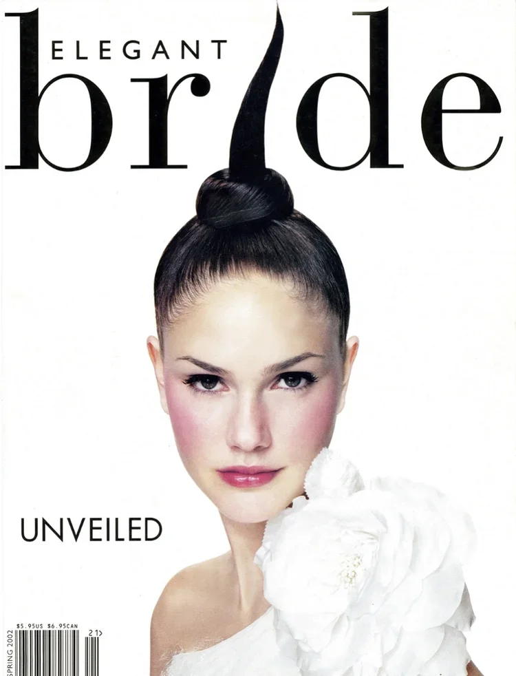 Cover of Elegant Bride magazine with a woman with dark hair in an updo and a tall hair accessory, wearing a white dress with large fabric flowers on the shoulder.