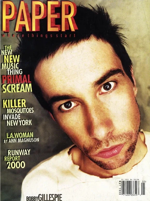 Magazine cover featuring a close-up of a young man with dark hair and beard, looking directly at the camera. The magazine title is 'PAPER' in large red and yellow letters. Additional text highlights topics like new music, primal scream, mosquitoes in