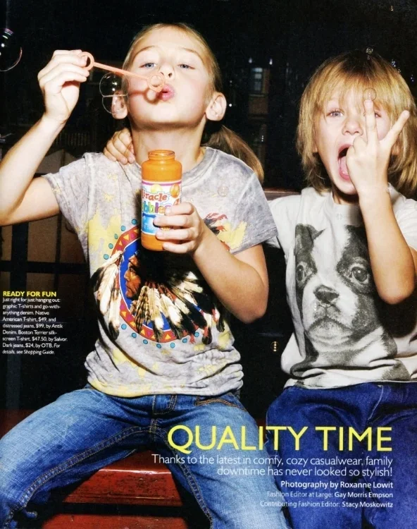 Two children sitting side by side, one girl blowing soap bubbles with bubblegum, the other making a peace sign with her fingers.