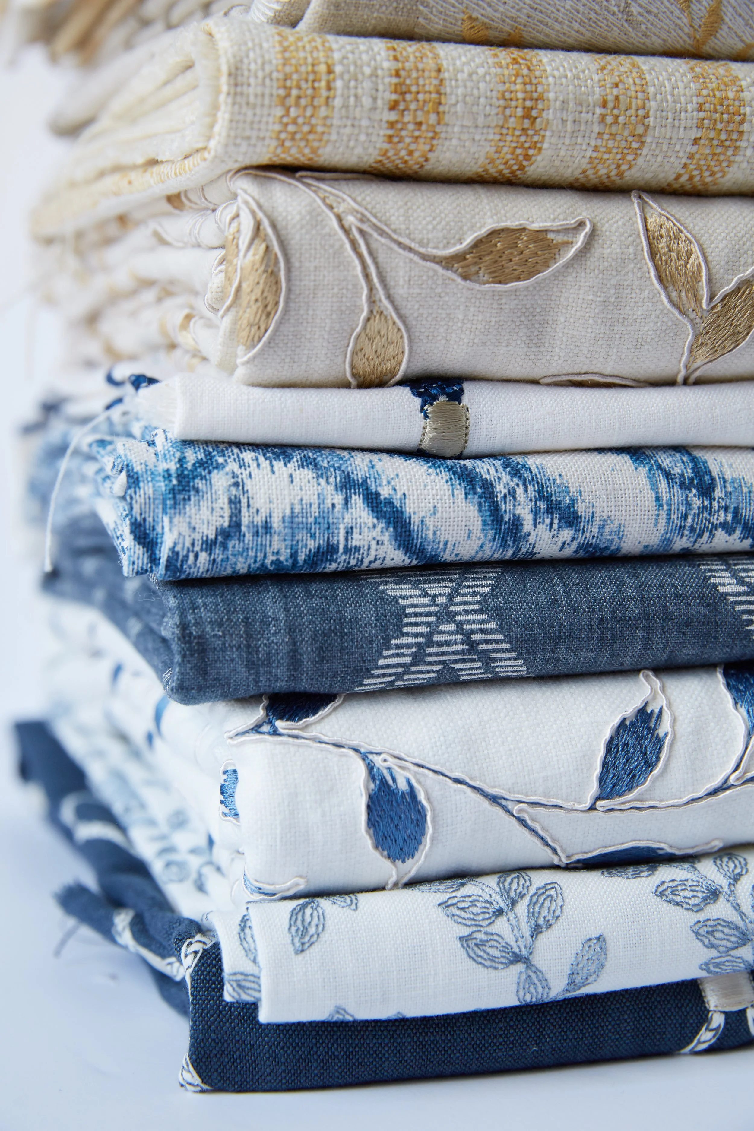 Stack of folded blue and white textiles with various patterns including floral, leaf, and geometric designs.