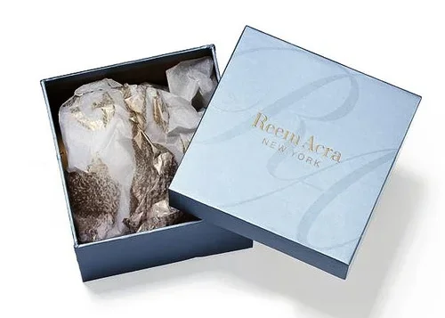 Open blue gift box with gold-foiled tissue paper inside, labeled Roem Arca New York.
