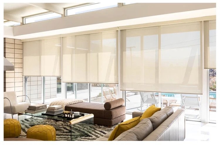 Bright living room with large windows and beige roller shades, modern furniture, and yellow accent pillows.