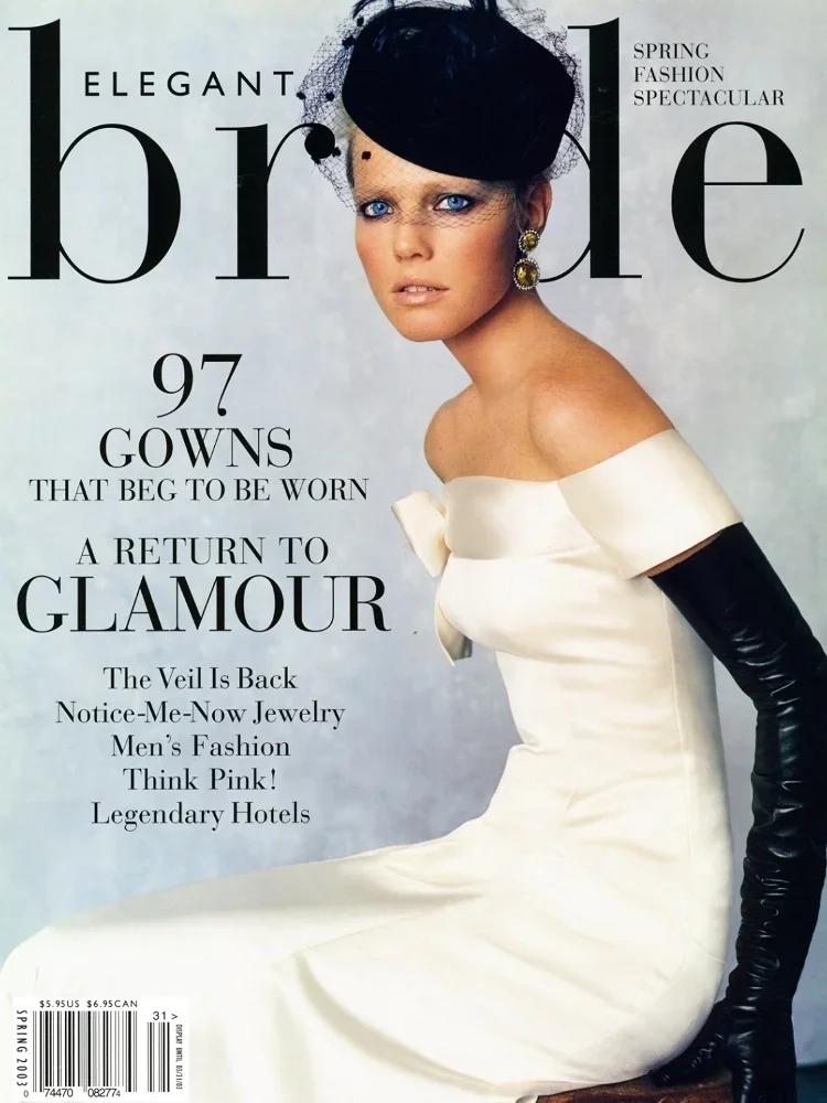 Cover of Vogue magazine featuring a woman in a white off-shoulder dress with long black gloves, wearing a black veil and earrings, and a matching black hat, with text about spring fashion and glamour