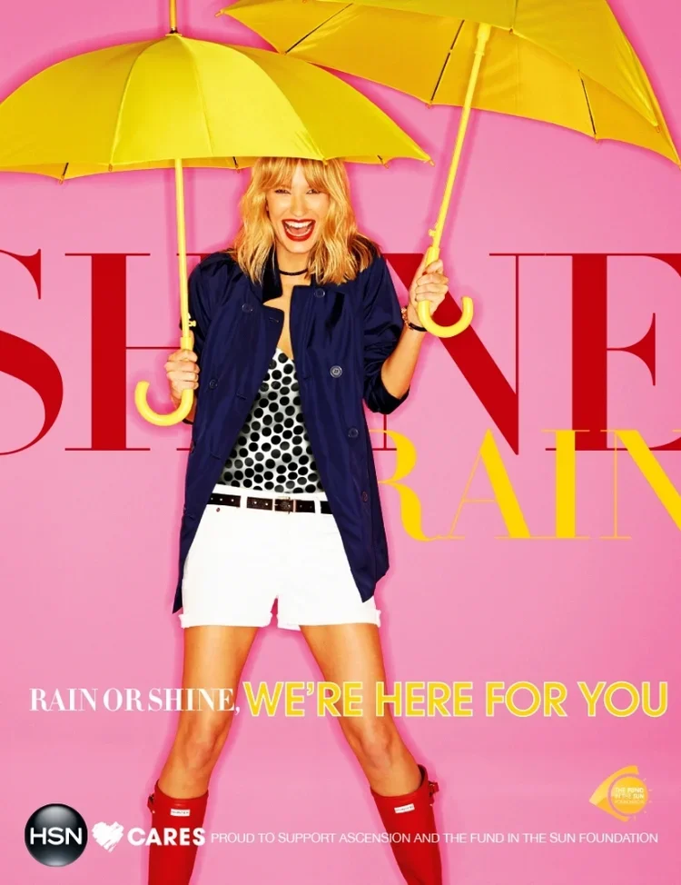 A woman with blonde hair, dressed in a navy jacket, polka dot top, white skirt, and red rain boots, holding two yellow umbrellas in front of a pink background with large red and yellow text.