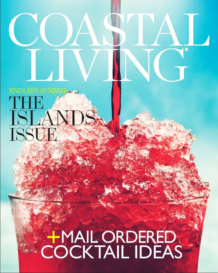 Coastal Living magazine cover featuring a large glass of red slushy cocktail topped with ice and red liquid pouring from above, with a light blue sky background. The magazine includes headlines about summer, island issues, and cocktail ideas.