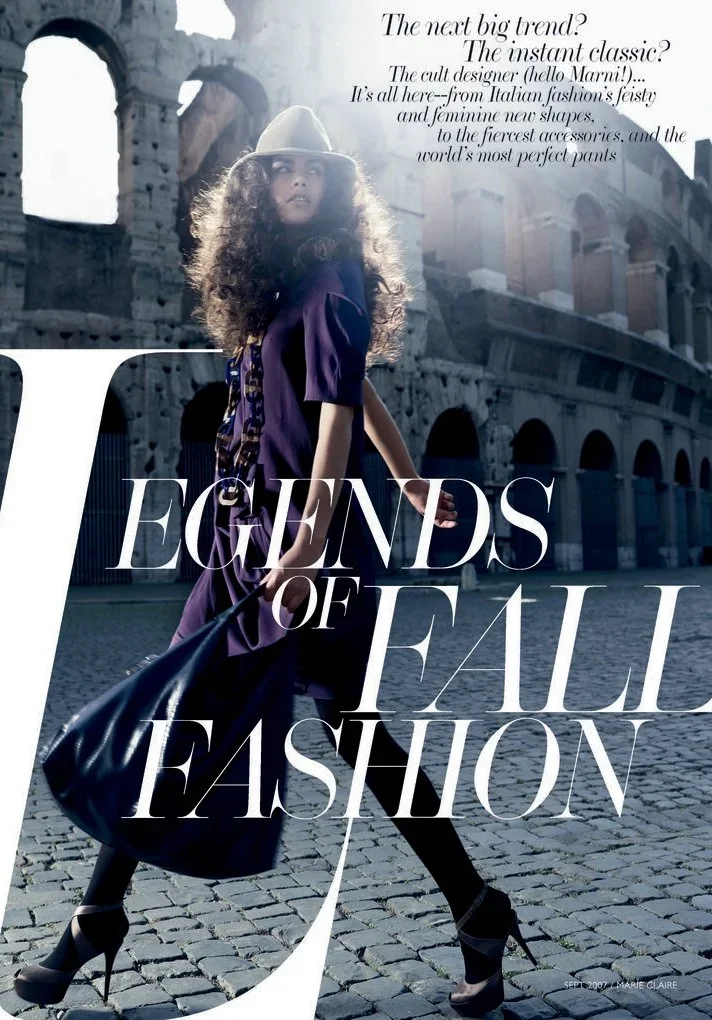 Fashion magazine cover featuring a woman with long curly hair wearing a wide-brim hat, purple dress, and high heels, standing in front of ancient Roman ruins, holding a black handbag. The cover headline reads 'Legends of Fall Fashion' with additional text about fashion trends.