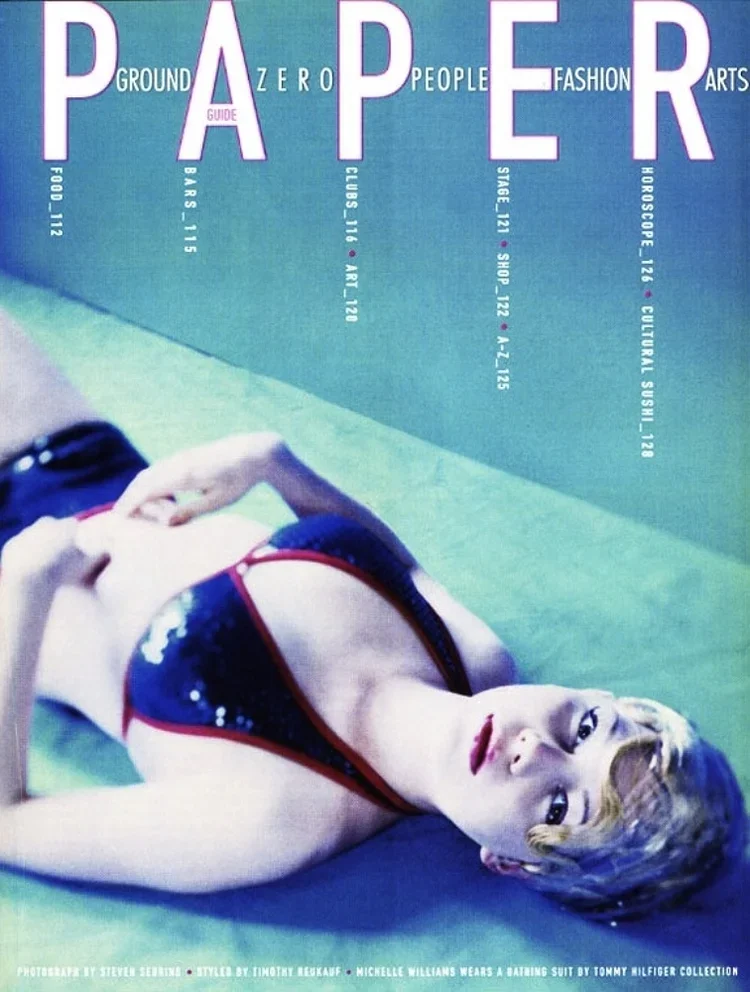 A woman with short, blonde hair lying on the floor, wearing a black and red swimsuit, looking at the camera, with magazine text overlaid.