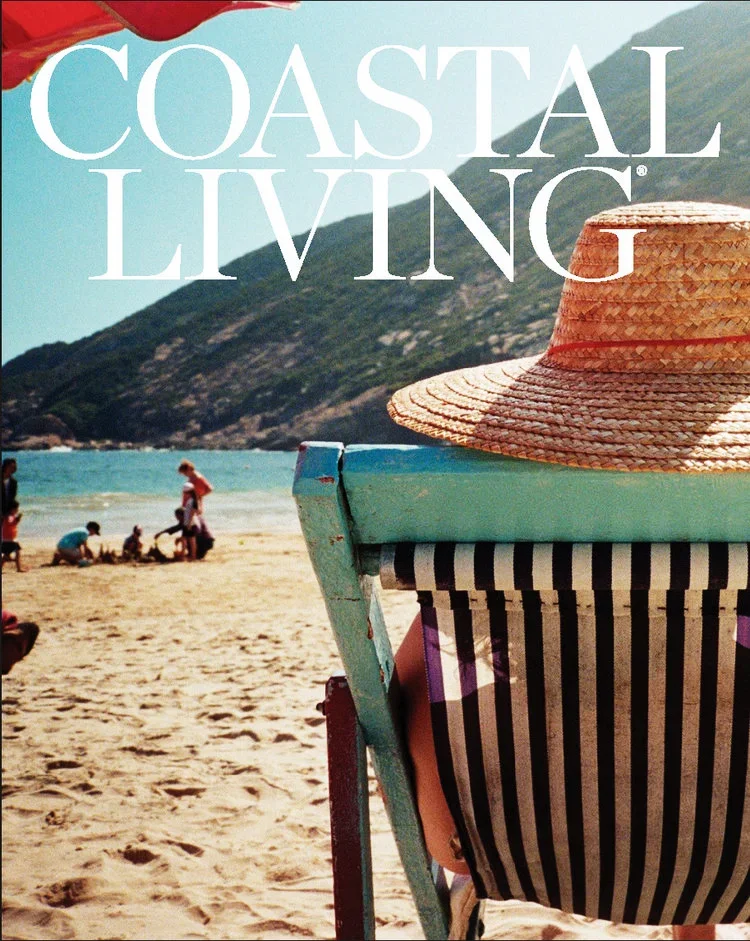 Beach scene with people and a mountain in the background, a striped beach chair, and a wide-brimmed straw hat. The text 'Coastal Living' is overlaid at the top.