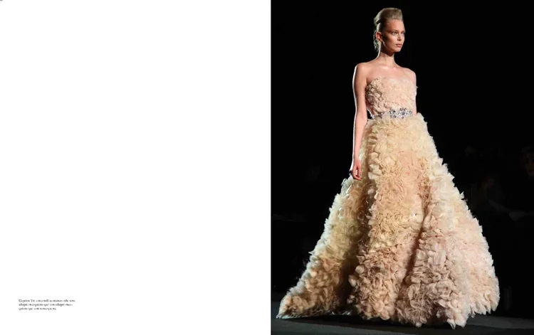 A fashion model walking down the runway in a strapless, floor-length gown with a textured, ruffled skirt and a fitted bodice with floral embellishments.