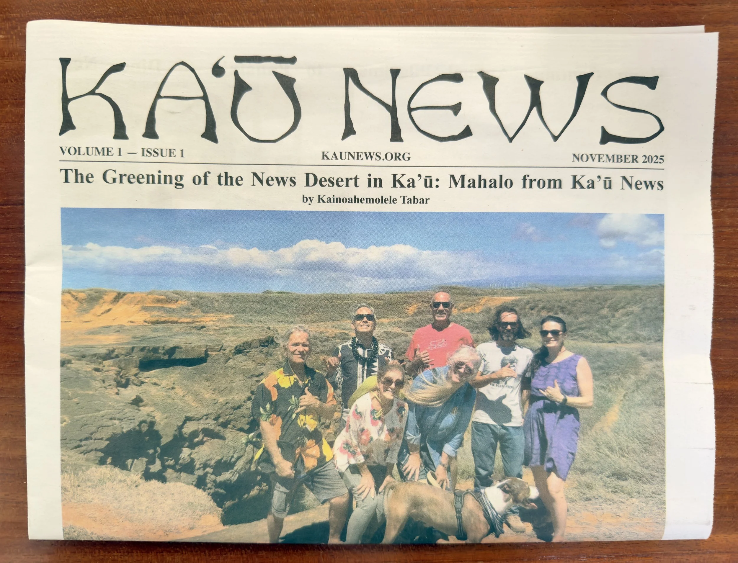 A printed newsletter titled "KA'Ū NEWS" from November 2025, featuring a story about the greening of the News Desert in Ka'ū and a photo of nine people posing outdoors in a rocky landscape under a blue sky.