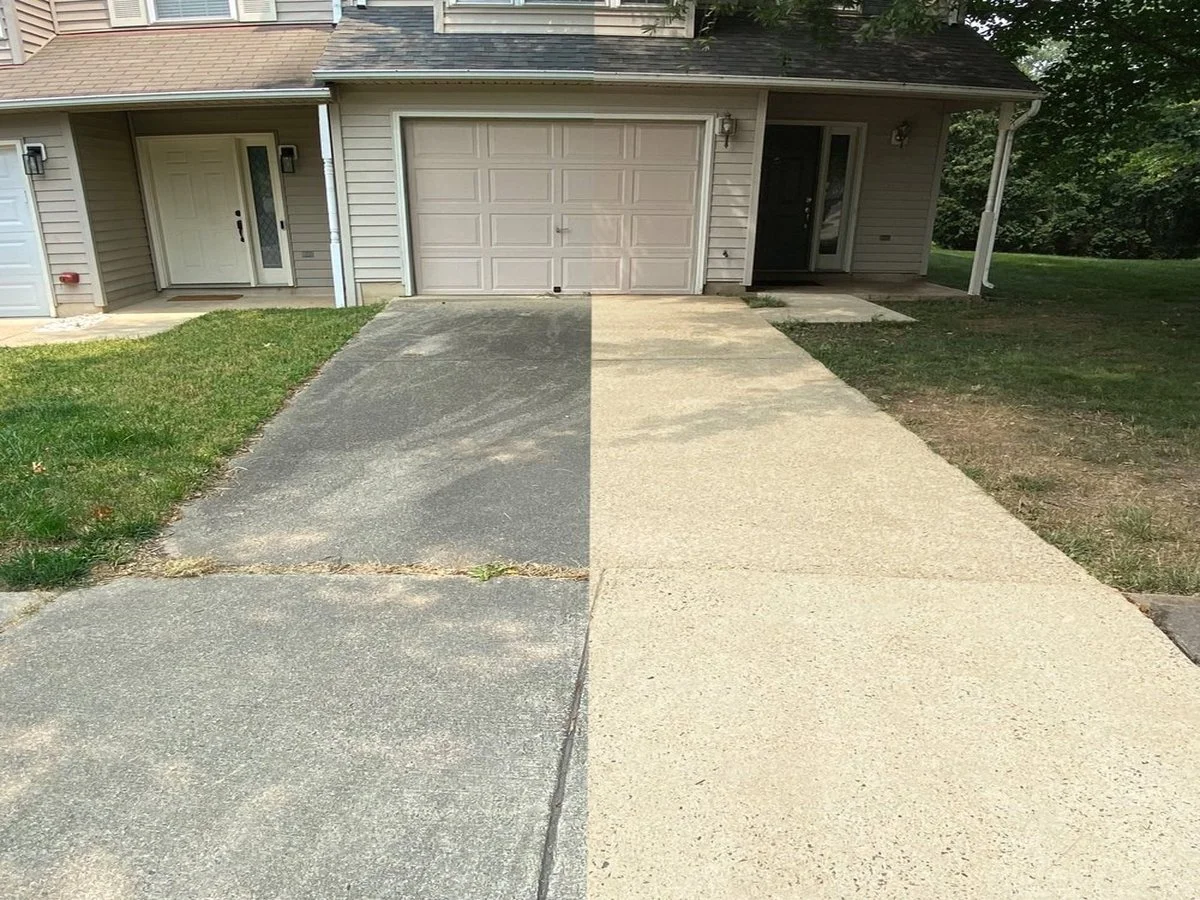 View of a house with a front porch, garage, and driveway, half of which is old and weathered gray concrete and the other half newly paved in light-colored concrete.