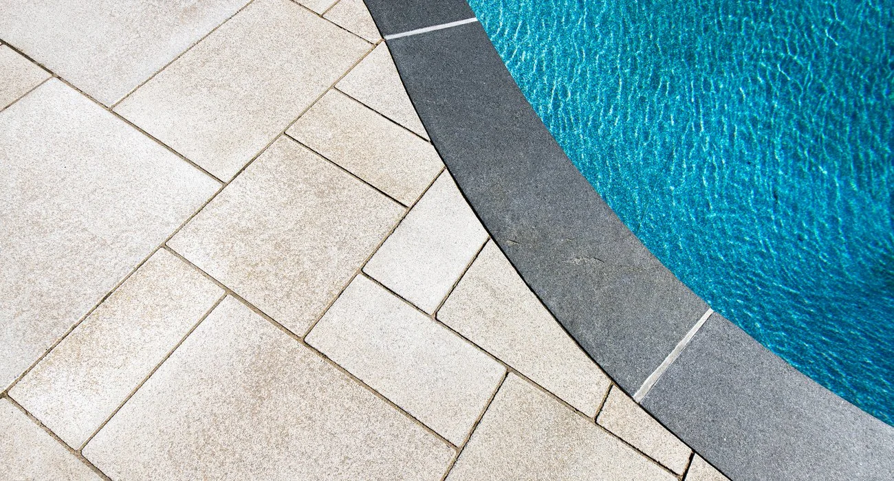 Close-up of a swimming pool with a textured blue surface, surrounded by beige and dark gray tiles.