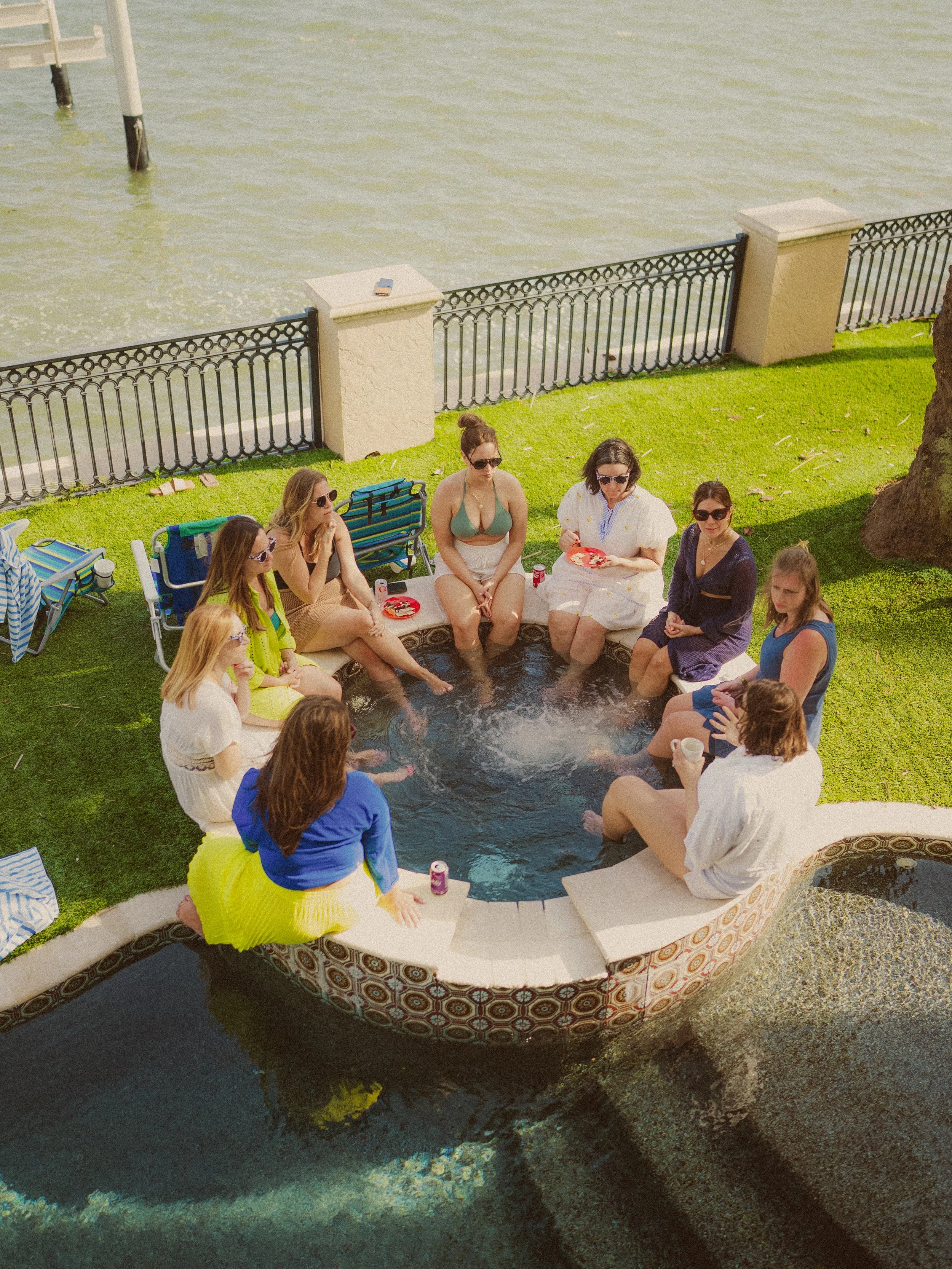 People sitting around a water feature in a backyard, with some feet in the water, enjoying a casual outdoor gathering.