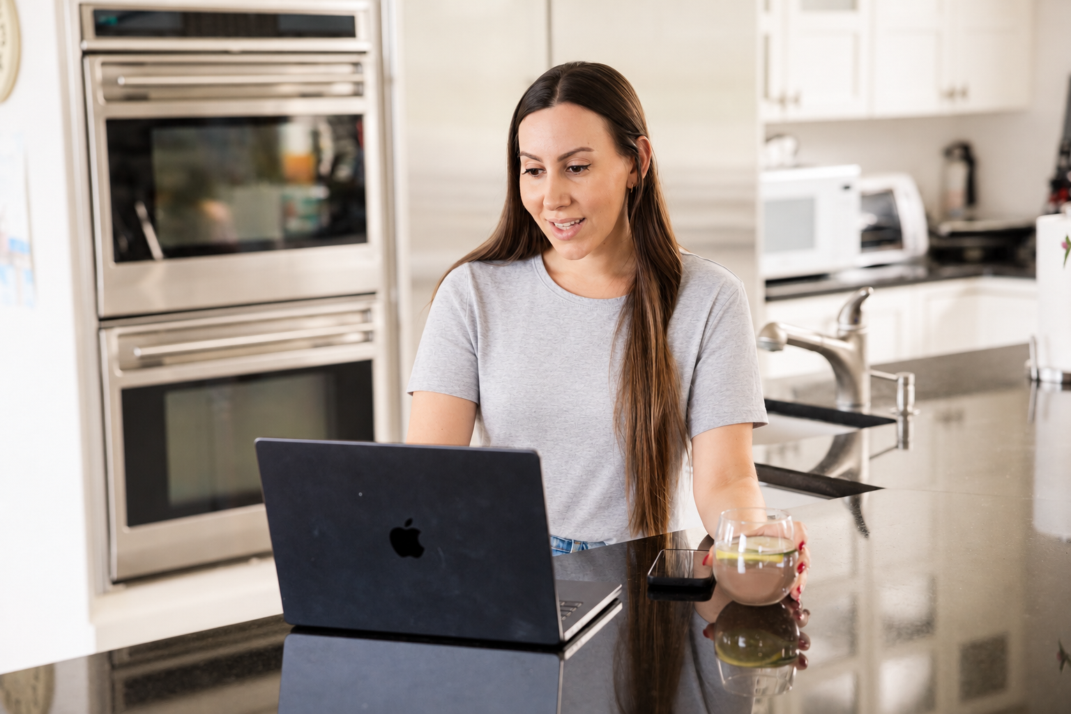 Woman using laptop in kitchen with coffee and smartphone