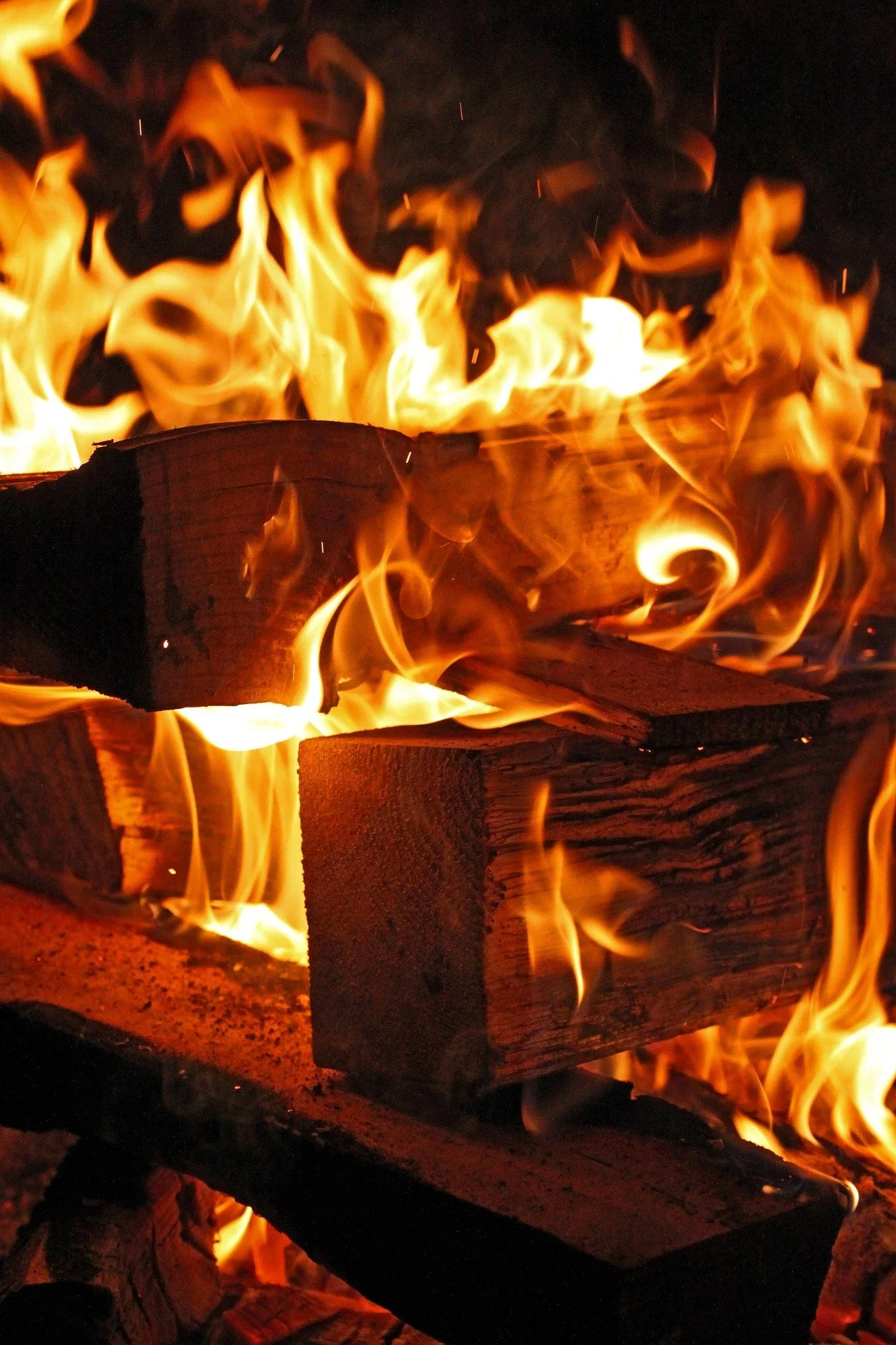 Wooden logs burning with bright orange and yellow flames against a dark background.
