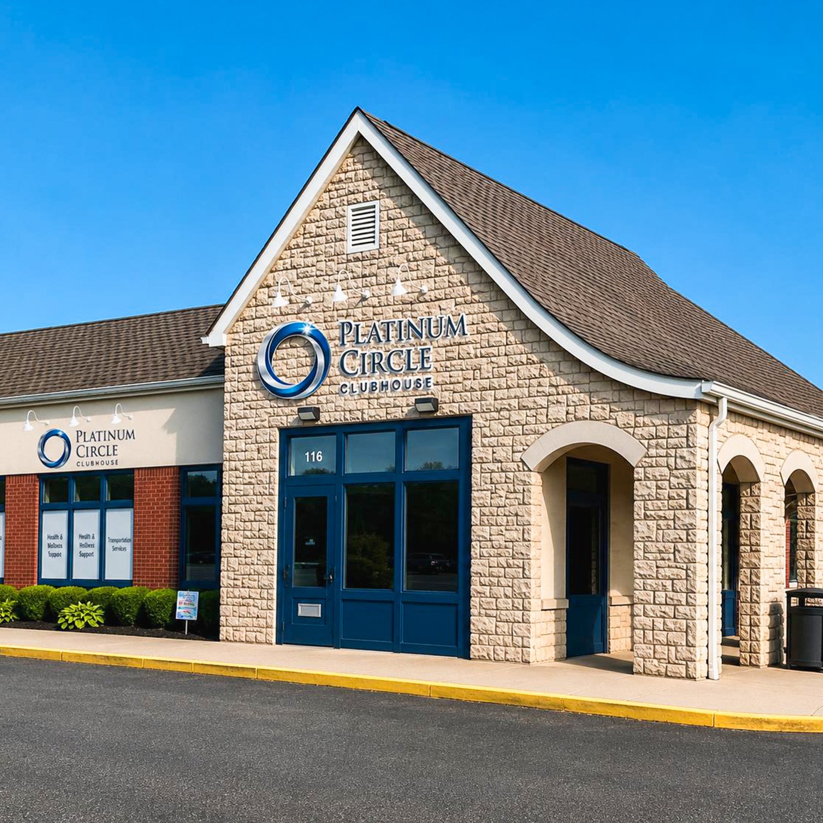 Front view of Platinum Circle Clubhouse with brick and stone exterior, blue doors, and a large sign, under a clear blue sky.