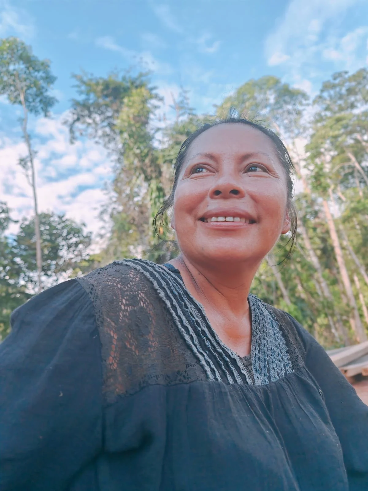 Portrait of Kichwa musician and artisan Samay Taky smiling outdoors beneath trees and a blue sky.
