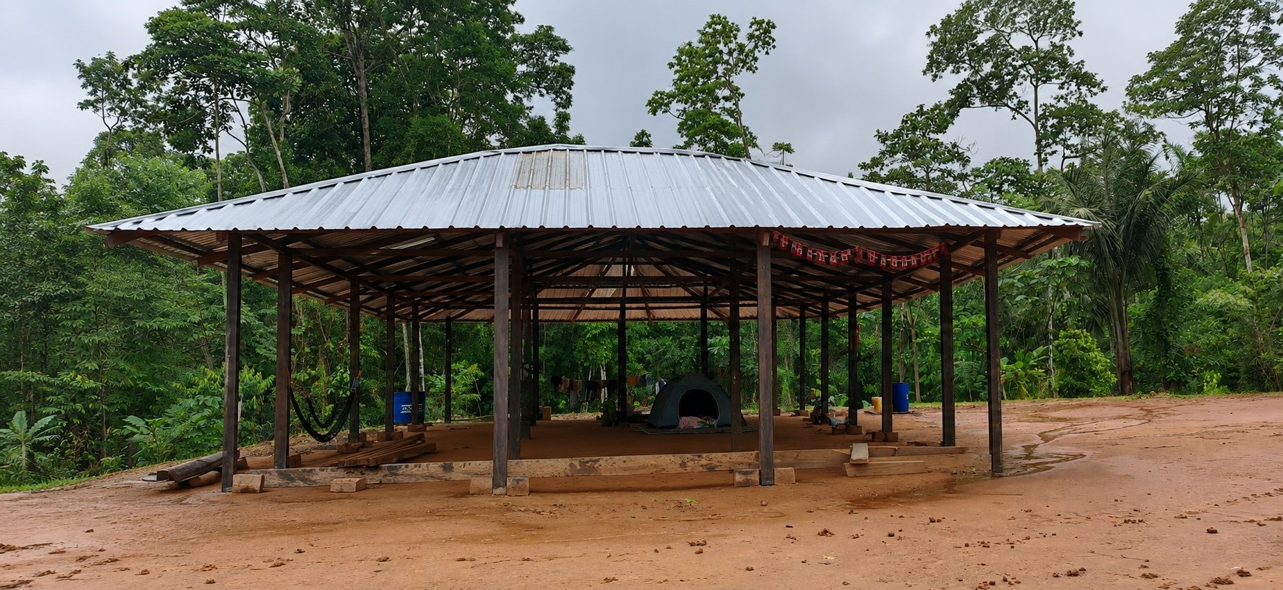 Community building under construction with a metal roof, surrounded by lush rainforest at Amarun Kucha.