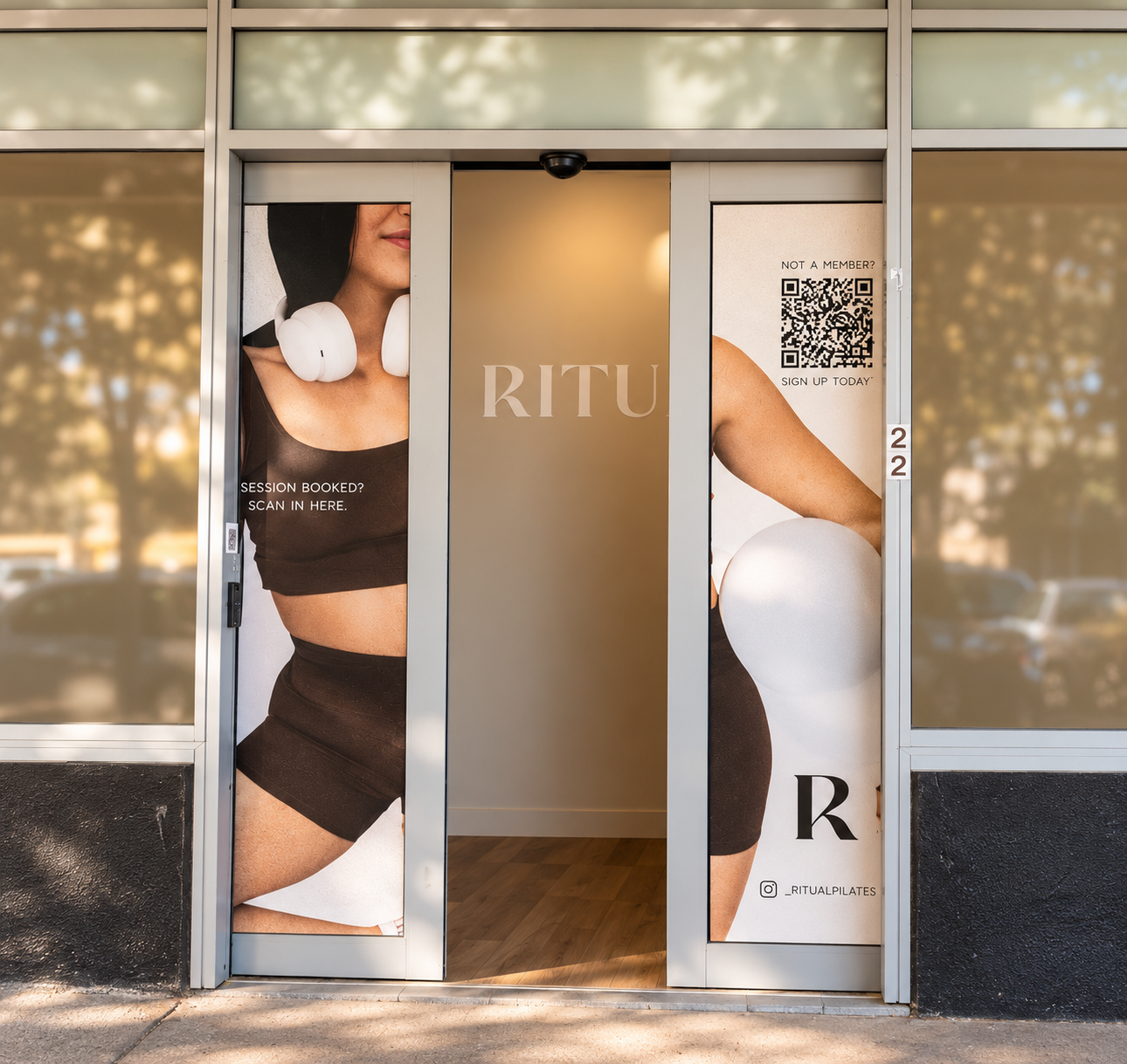 Glass door with large advertisements for Ritual Reformer Pilates studio. On the left, a woman wearing black workout wear and white headphones. On the right, a woman stretching with a white ball. Entrance to Linkd Studio. 22 Arawa Street, Matamata