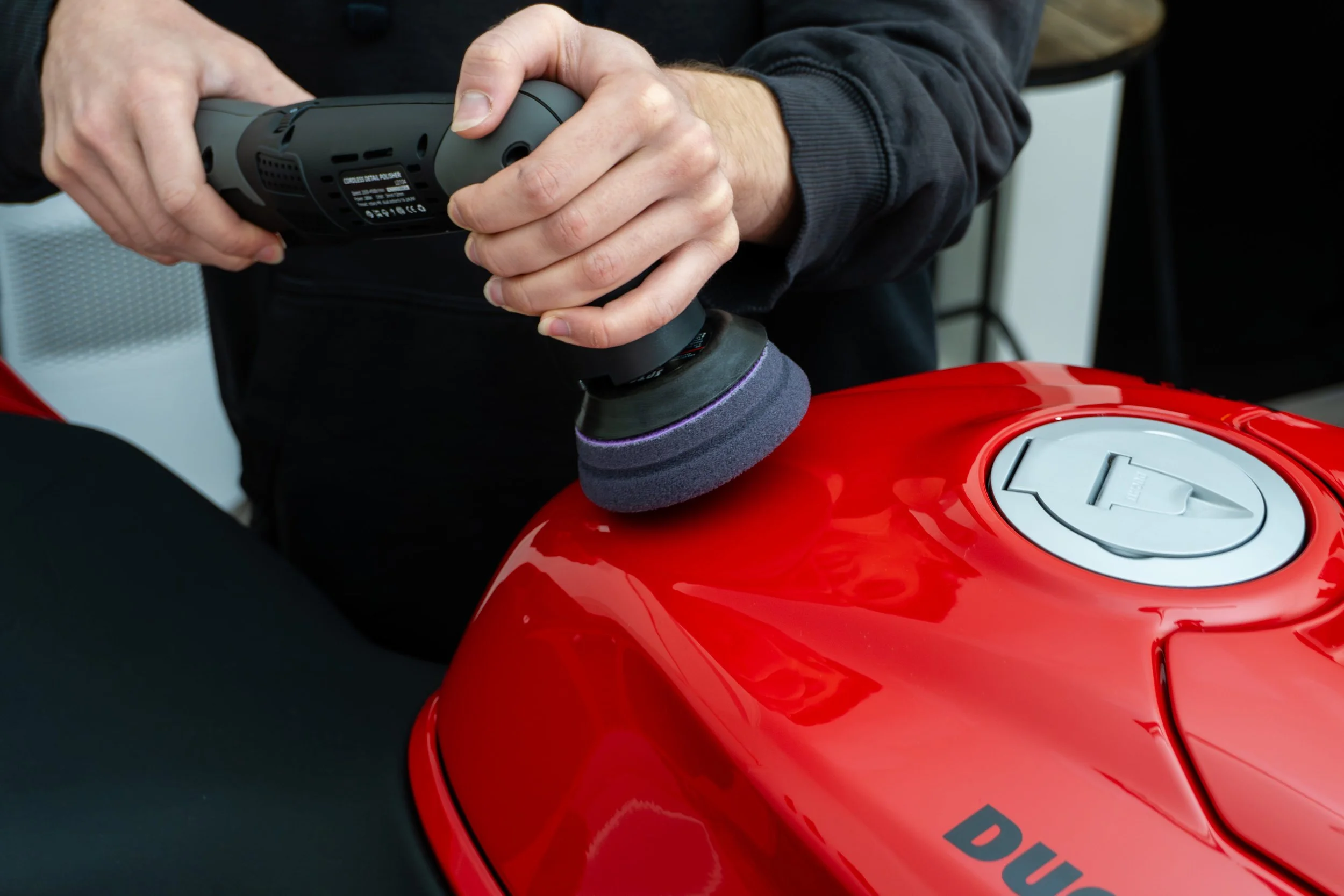 Professional detailer using a handheld electric polisher on a red motorcycle fuel tank, in Cheltenham, Melbourne.