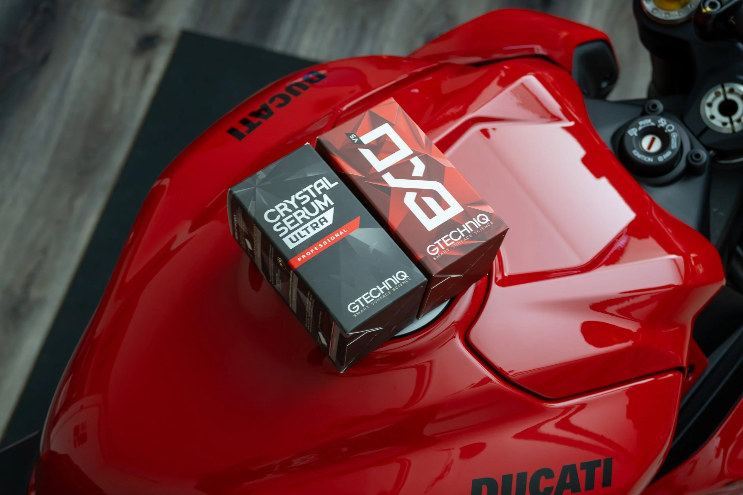 Close-up of a red motorcycle's fuel tank with two boxes on top labelled 'Crystal Serum Ultra' and 'EXOv5': Gtechniq's professional ceramic coating products.