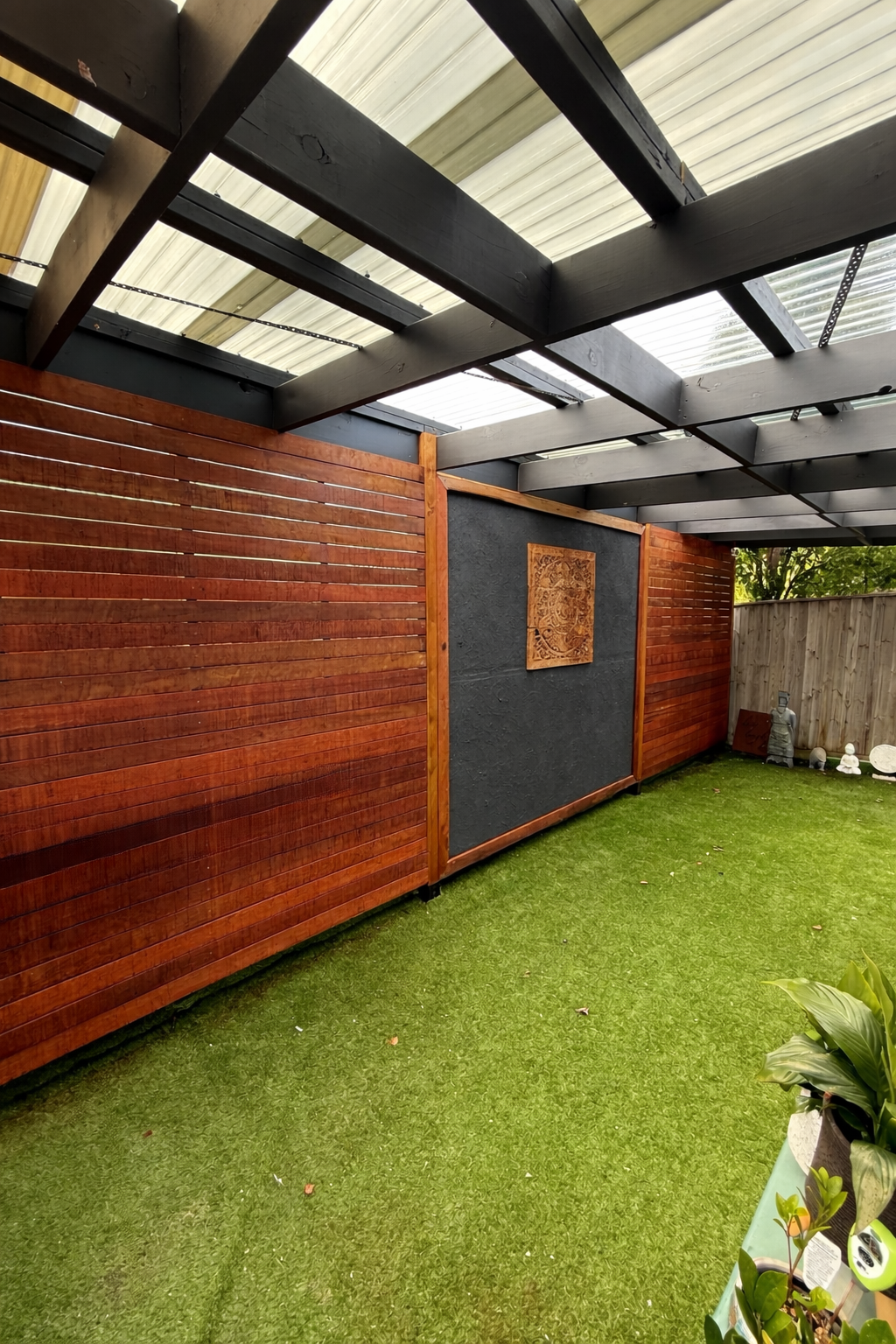 Small backyard garden with a green lawn, wooden fence, and a decorative wooden sculpture on the wall.
