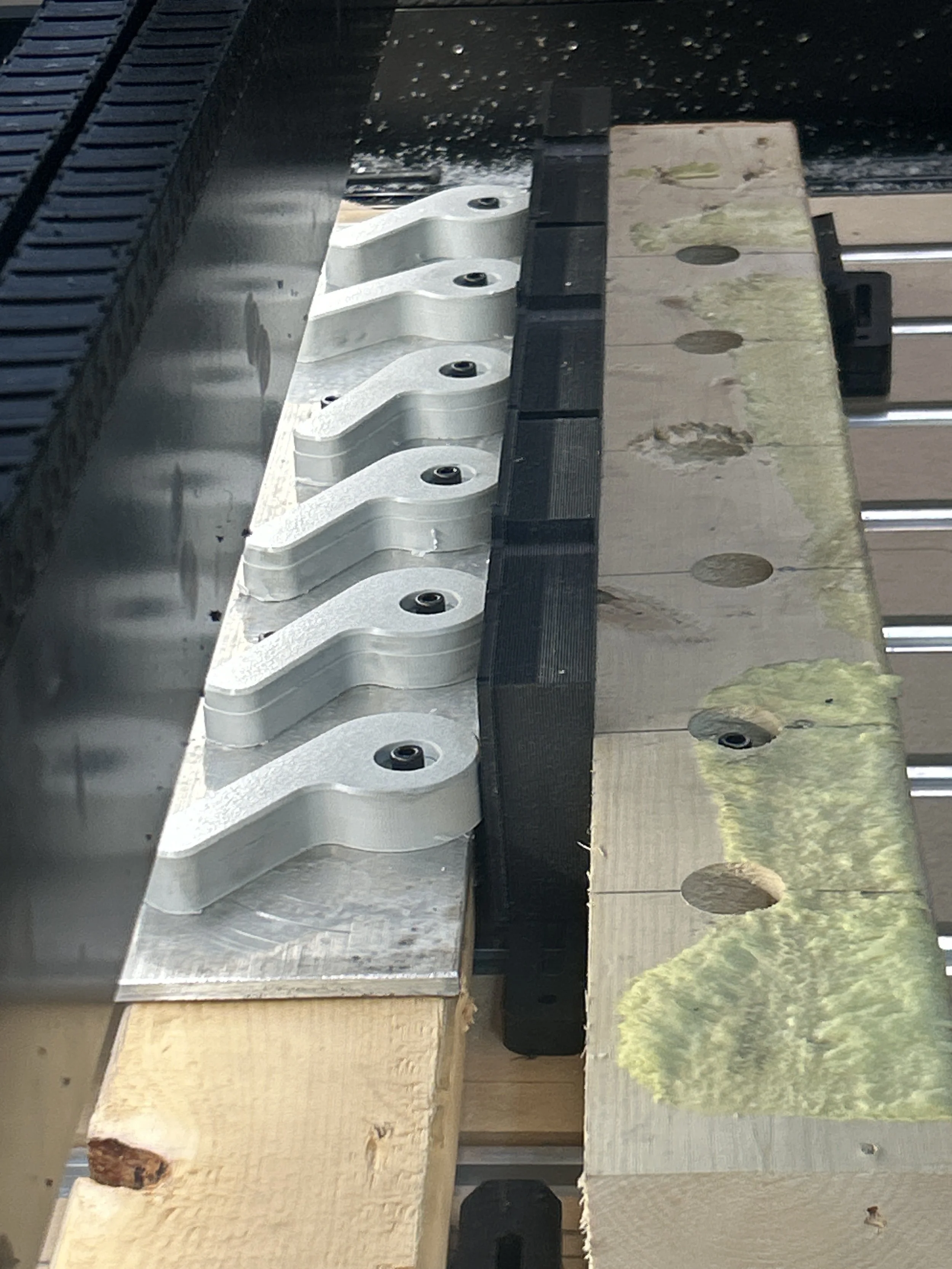 Close-up of a metal machine part and wooden plank with holes, outdoors environment reflected on the surface.