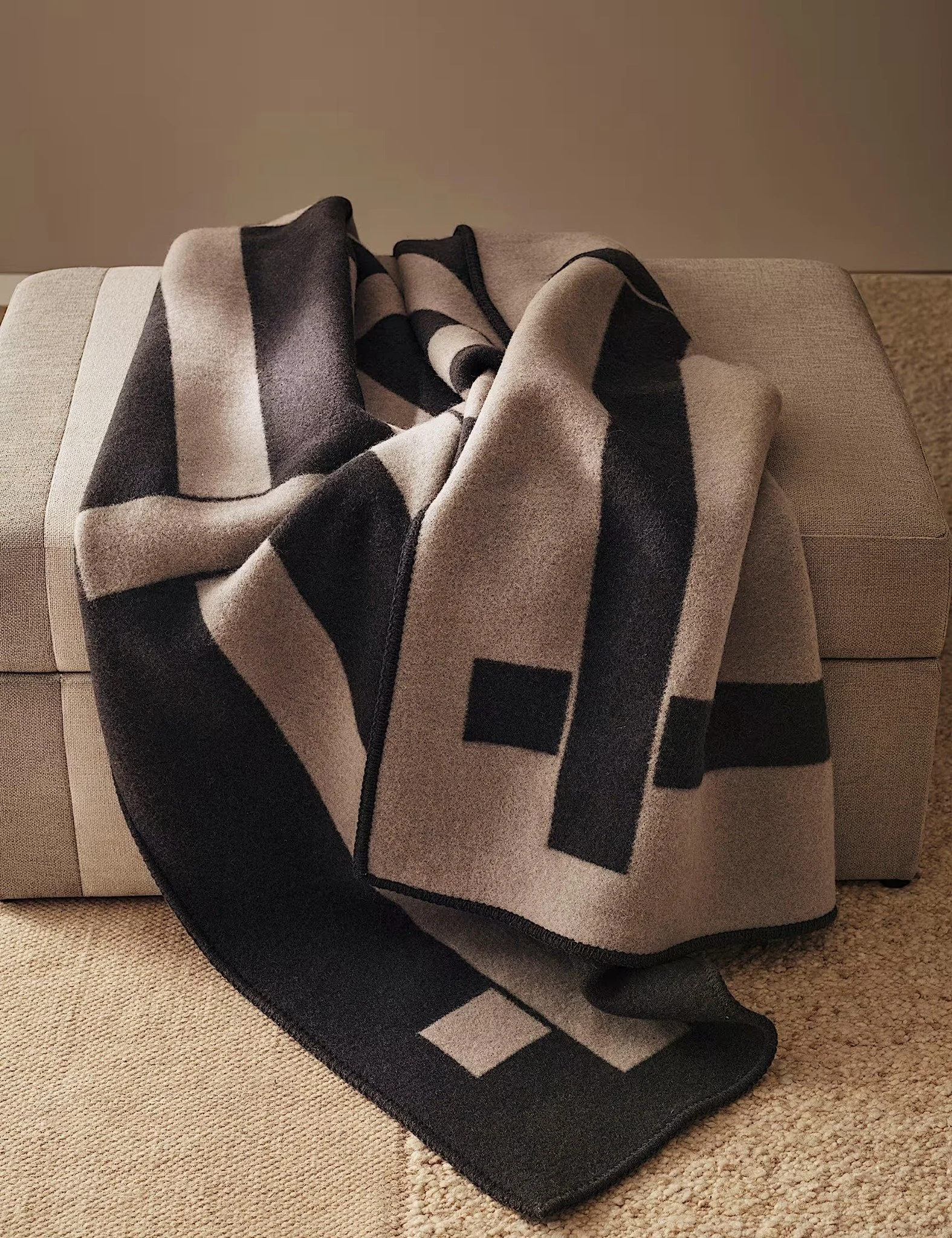 A beige sofa with a black, white, and gray striped blanket draped over it, setting on a beige carpet.