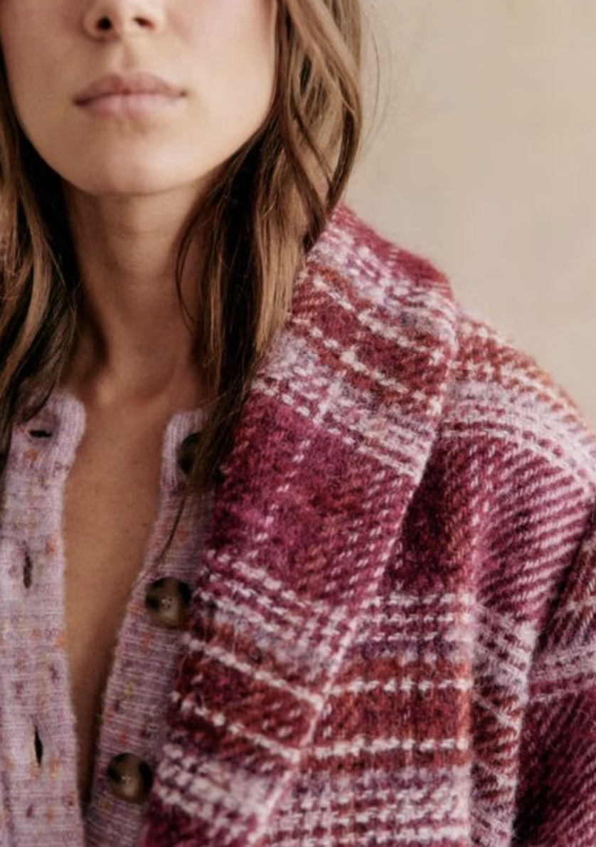 Close-up of a woman's face and shoulder, wearing a red and white patterned cardigan.