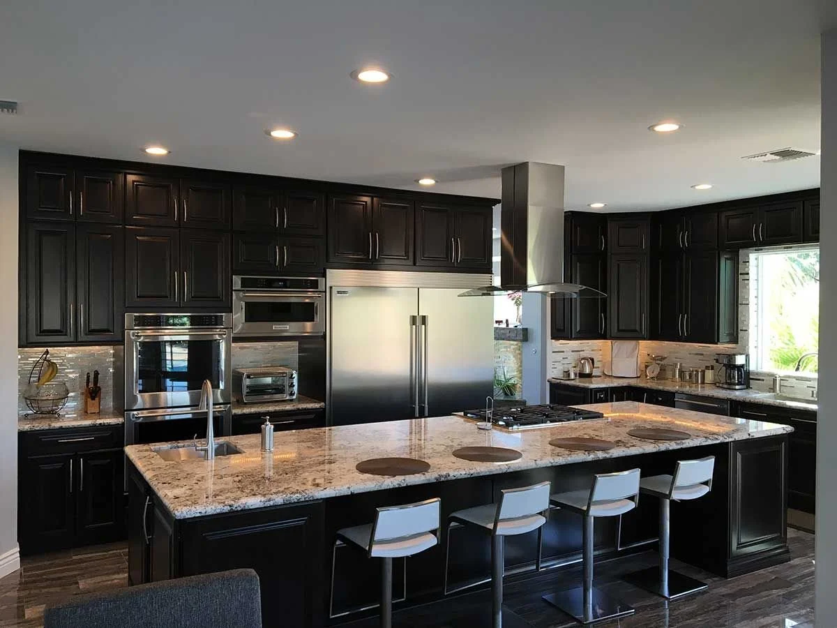 Modern kitchen with dark wood cabinets, stainless steel appliances, granite countertops, and a large island with four white bar stools.