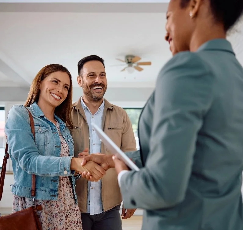 A woman and a man shaking hands with a realtor while smiling.