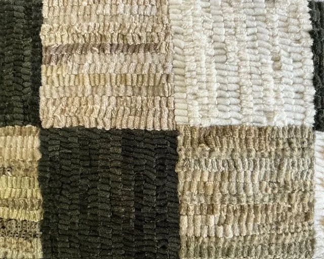 Detail of hand-hooked wool texture forming the checkerboard pattern.
