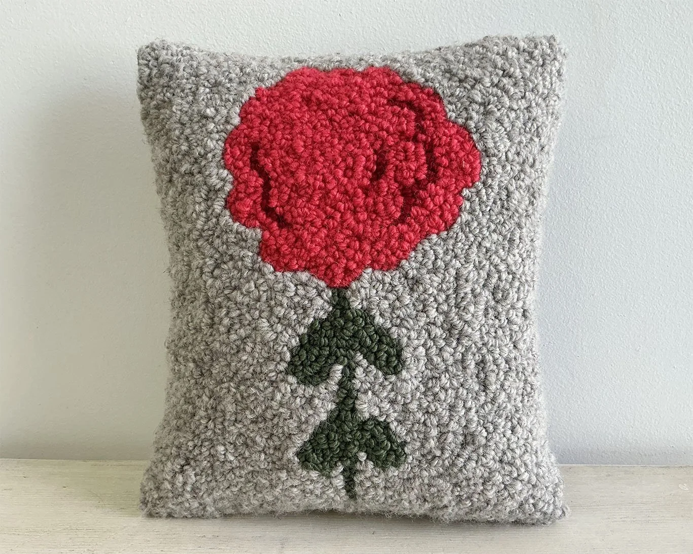Gray hand-hooked wool pillow with a bright pink stylized alpine flower motif.