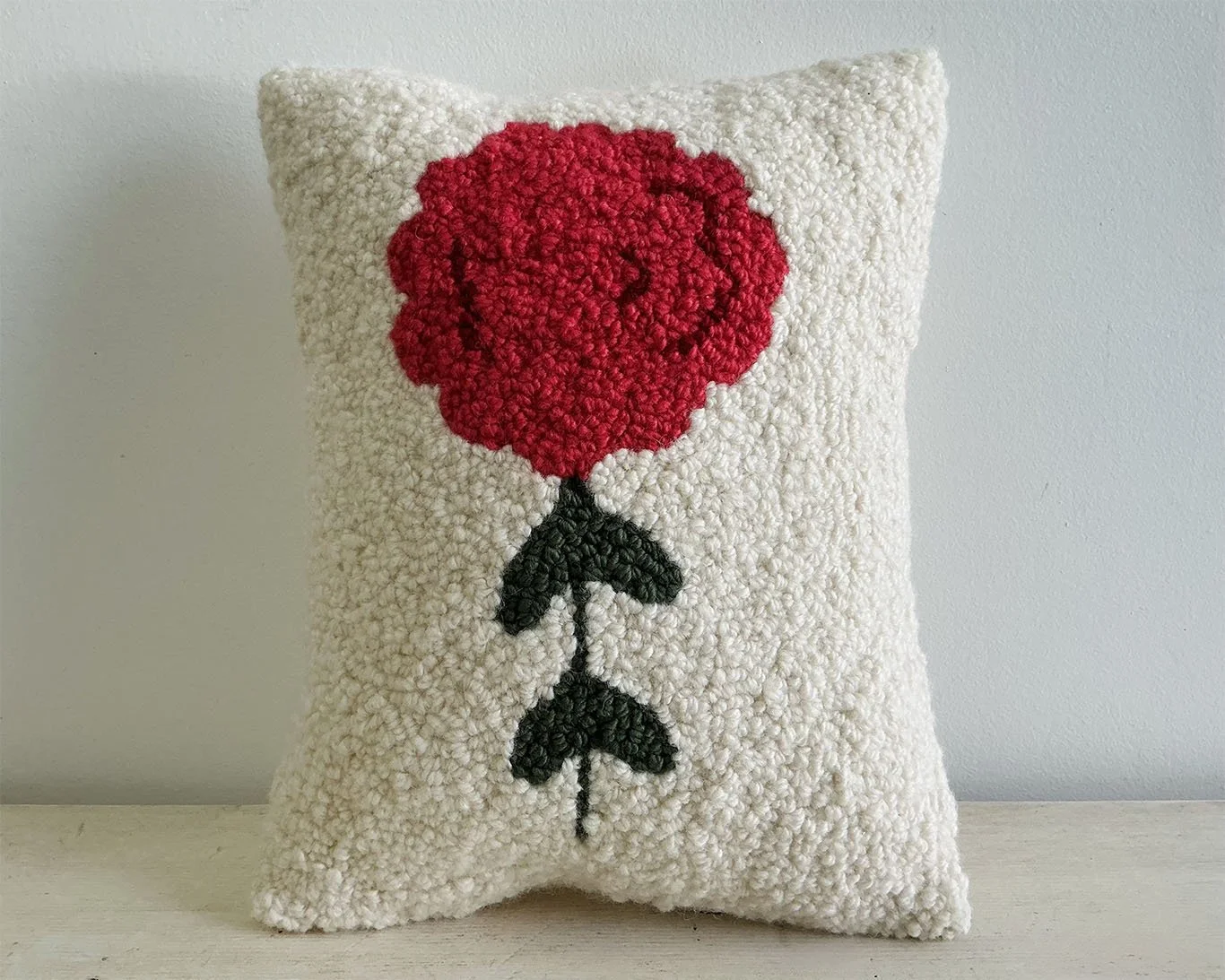 Ivory hand-hooked wool pillow with a crimson stylized alpine flower motif.