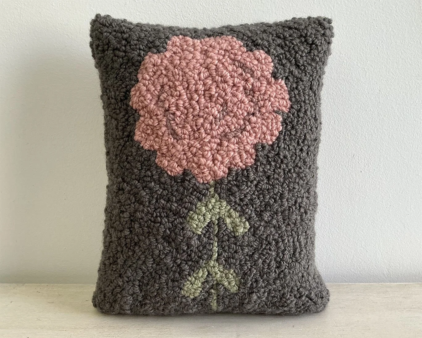 Gray hand-hooked wool pillow with a pink stylized alpine flower motif.