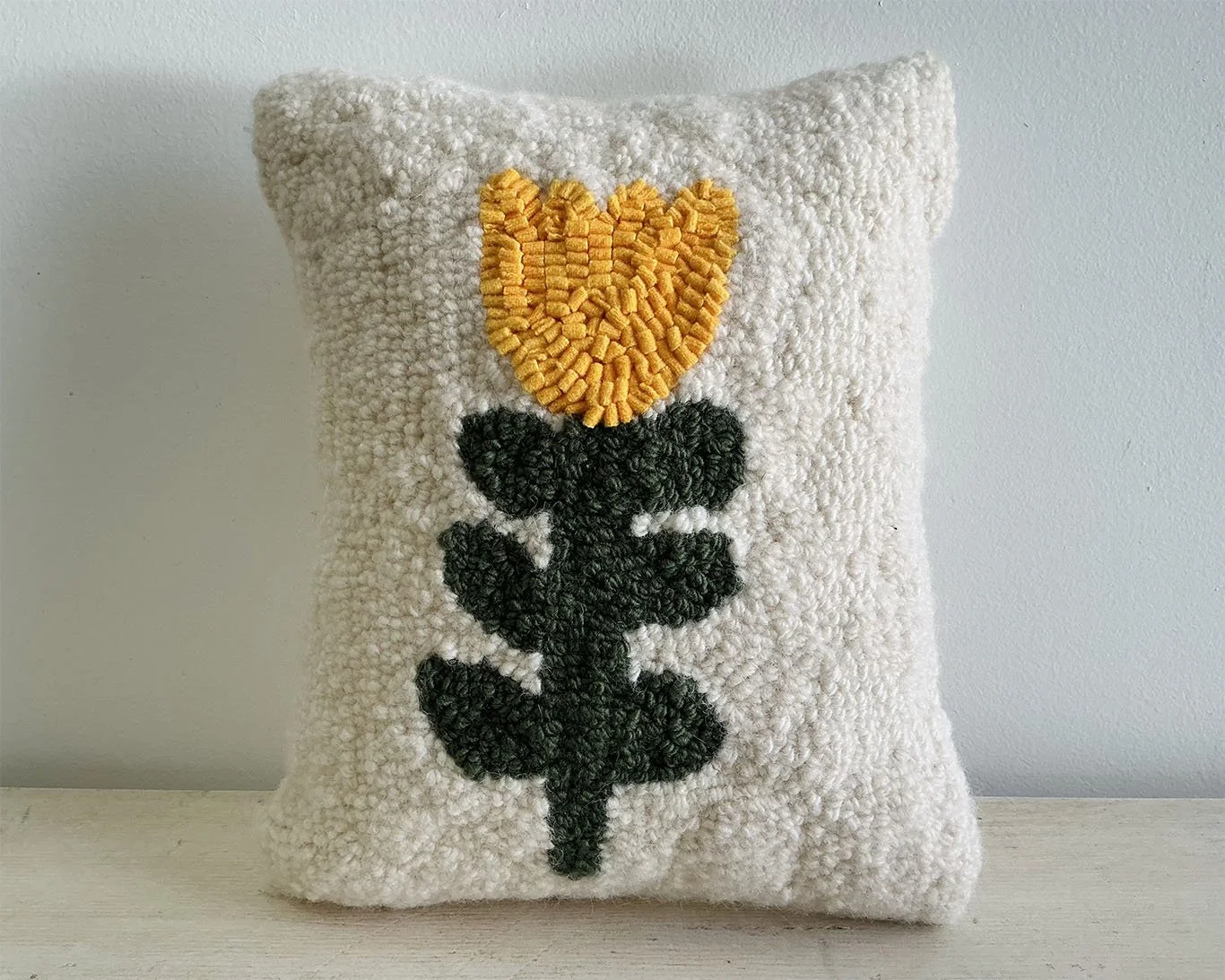 Ivory hand-hooked wool pillow with a yellow stylized alpine flower motif.