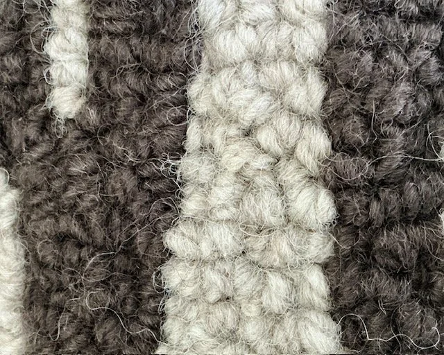 Detail of hand-hooked brown wool letters against softly variegated granite background.