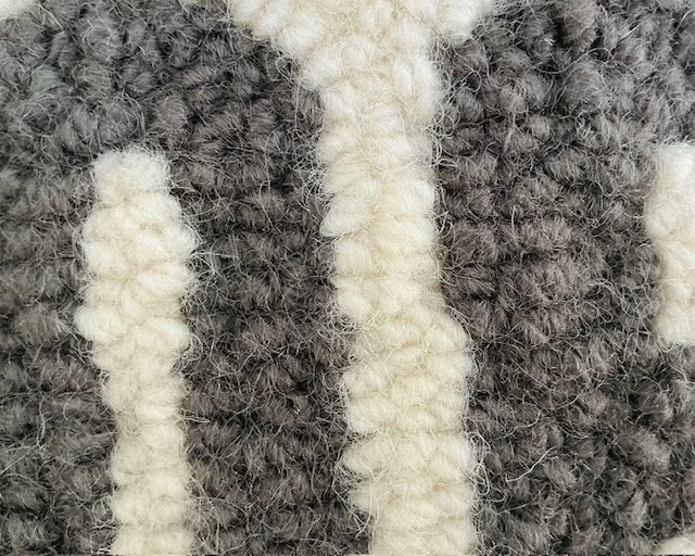 Detail of hand-hooked wool showing charcoal lettering against the natural ground.