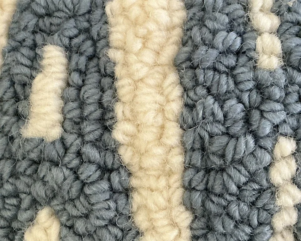 Detail of hand-hooked wool showing blue lettering against the ivory ground.