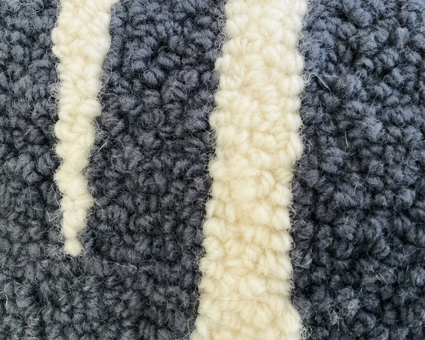 Close-up of hand-hooked wool loops showing slate and bone-colored fibers and the textured letterform surface.