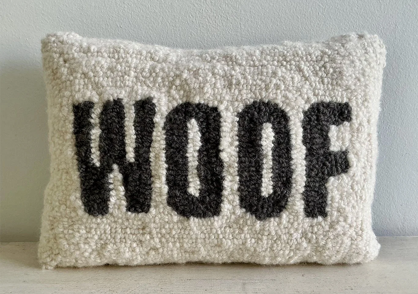 Natural hand-hooked wool pillow with the word "WOOF" in charcoal lettering.