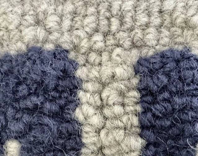 Detail of hand-hooked wool showing indigo lettering against the natural stone ground.