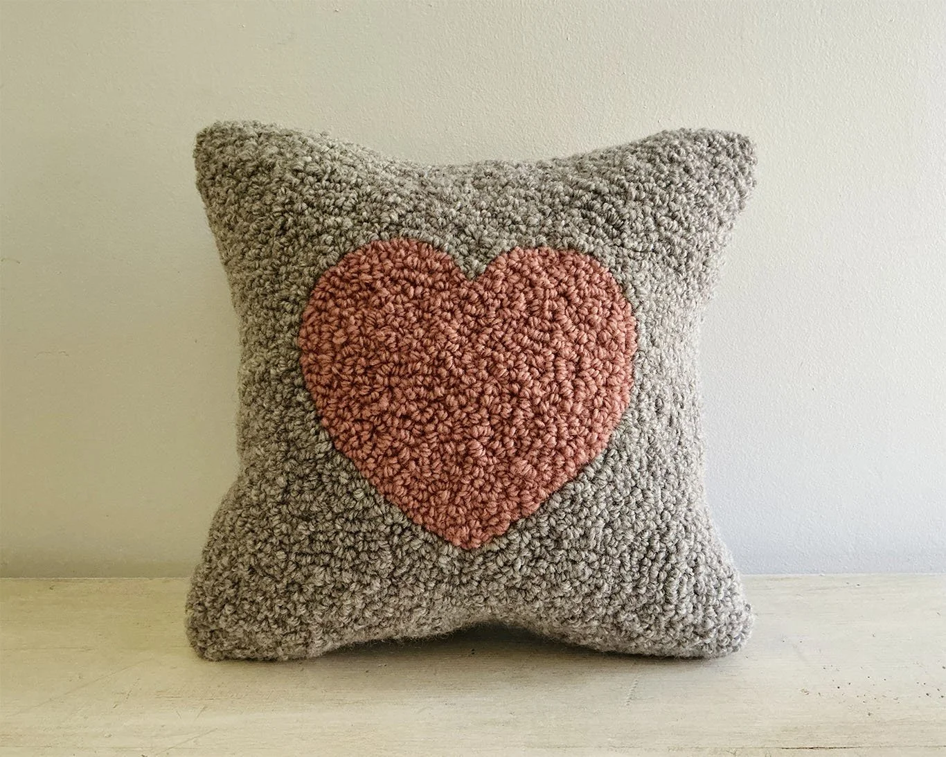 Hand-hooked wool pillow with a blush-pink heart centered on a stone-gray wool ground.